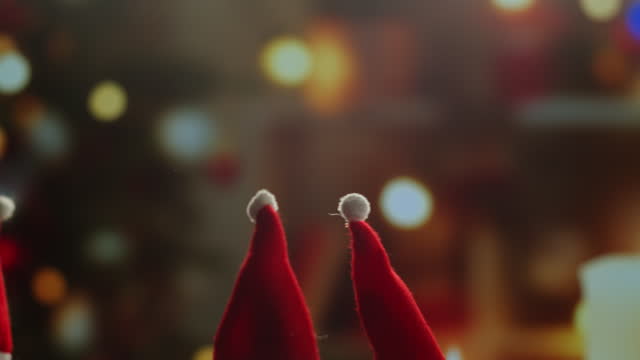 Little Christmas hats on background close-up. Elfs, dwarfs in red hats walking at home near christmas tree. Vibes of winter holidays,2024, 2025