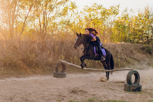 Young woman and her horse jump large jump while riding.