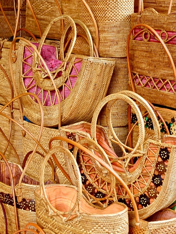 Vertical closeup photo of a variety of handwoven natural fibre baskets with handles piled onto a stall at the daily Craft Market in Ubud, Bali.