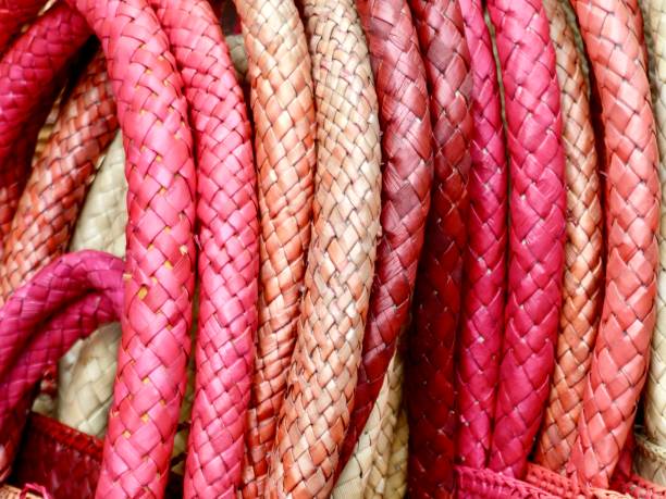 Horizontal extreme closeup photo of cream and pink coloured hand woven fibre handles on a stack of baskets for sale on a craft stall at the daily market in Ubud, Bali.