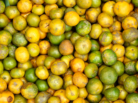 Horizontal high angle extreme closeup photo of a pile of green, orange and gold mandarins on display for sale on a food stall at the Ubud Food Market, Ubud, Bali.