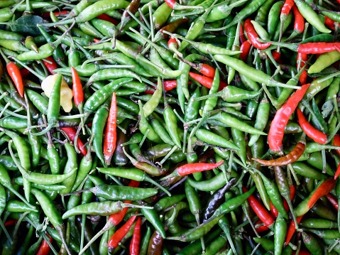 Horizontal high angle closeup photo of a heap of freshly harvested small, thin, red and green Chilies for sale on display on a food stall at the Ubud Market, Ubud, Bali.