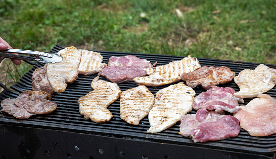 Man cooking (man's hand) meat on barbecue grill at barbecue party in summer garden. Food, people and family time concept. Pork - pork neck grilled on charcoal. Grilling time! Different types of meat on the grill.