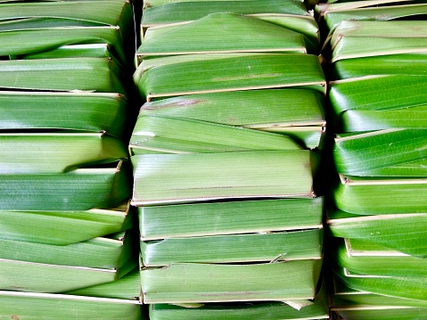 Horizontal extreme closeup photo of stacks of dried green coconut palm leaf offering baskets used to hold flowers, food, incense or sweets for religious ceremonies , for sale on a stall at the Ubud Food and Craft Market, Bali.