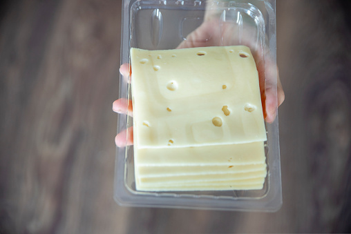 A woman's hand takes a piece of cheese from a pack close-up. Preparing for Cheese Lovers Day. High quality photo