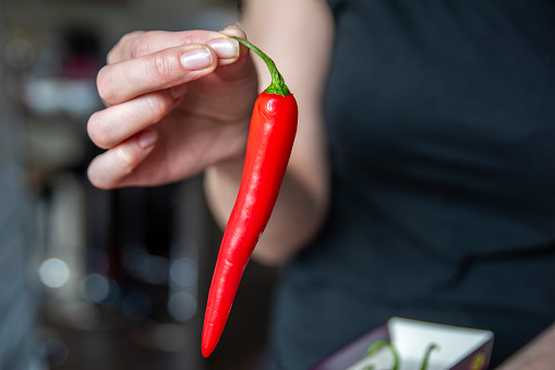 Woman's hand holding chili pepper close-up. Start cooking the spicy soup. High quality photo