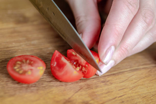 istock A hand cuts a cherry tomato with a knife close-up. Preparing salad to set the table. 1782361471