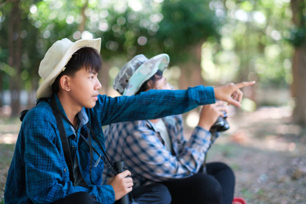 deux jeunes garçons à l’extérieur dans la forêt font de la randonnée et du camping, du scoutisme, de l’apprentissage de la faune, de l’utilisation de jumelles pour rechercher des animaux avec des amis. joyeuses vacances d’été souriantes et e - discovery binoculars boy scout searching photos et images de collection