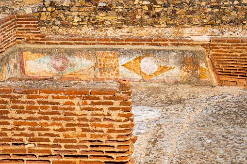 Restored ruins of ancient geometric Roman paintings and frescoes and eroded earthy orange colors from the Mitreo Roman House of the Archaeological Complex of Mérida, Spain.