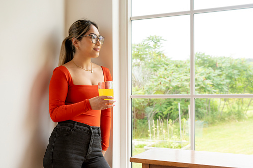 A young woman of Asian heritage enjoying an orange juice vitamin c drink at home.