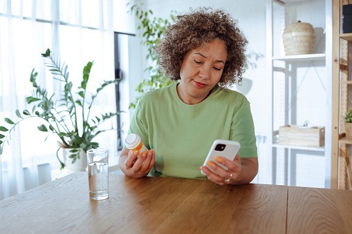 Mature African-American woman is at home, she is searching information's about medicine on smart phone