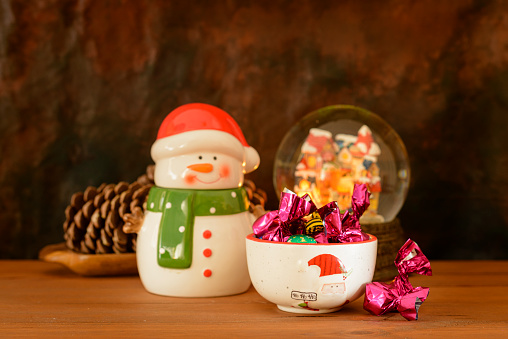 Christmas still life with porcelain figures and other objects, sweets and chocolates, on a wooden table with a dark background.