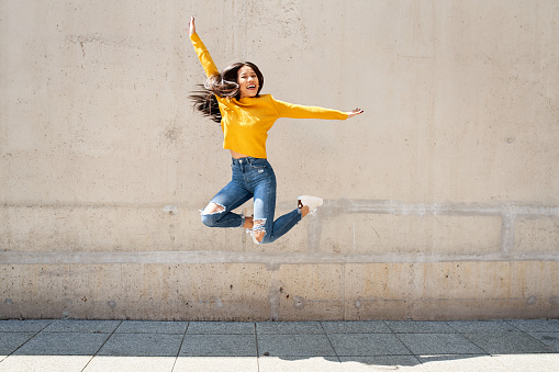 Joyful young woman jumping agains concrete wall