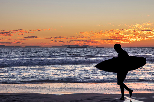 A surfer walking on the shore during the sunset