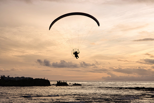A paraglider flying over the sea during sunset