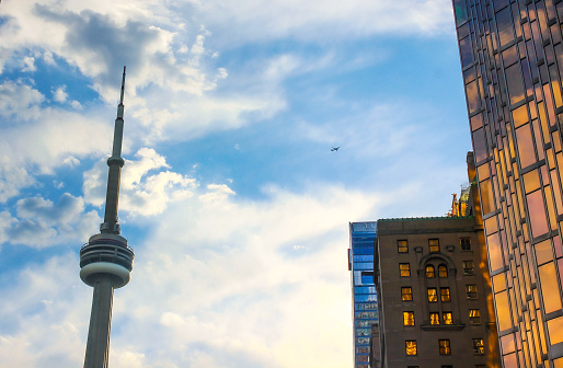 September 2023- Toronto, Canada: View on the Canadian National - CN - Tower (communications tower), taken from downtown Toronto by Union Station, with beautiful skies shortly after rain and the beginning of sunset and an airplane flying over.