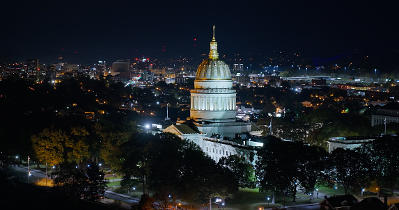A high angle aerial still photo of the West Virginia State Capitol building on a cold, fall night, with Charleston visible in the background.