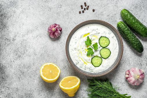 Tzatziki Greek sauce in a bowl with ingredients. Gray rustic background. Top view, flat lay, copy space