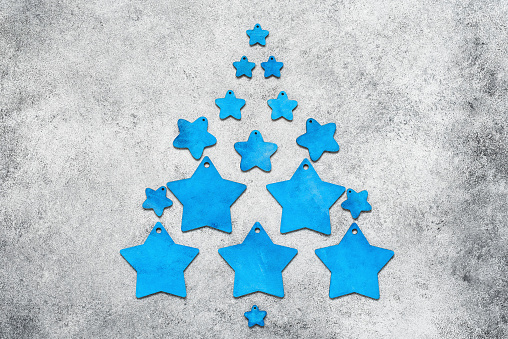 Blue wooden stars in the shape of a Christmas tree on a gray rustic background. Top view, flat lay.