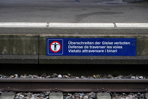 Banner with a pictogram saying it is forbidden to cross the tracks at the railway station in Urdorf, Switzerland. The warning is written in German, French and Italian languages.