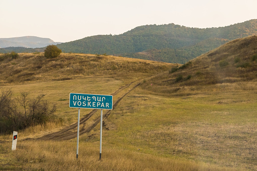 Voskepar, Armenia - 01 September 2019: Road sign with the name of the town of Voskepar. Mountains in the background.