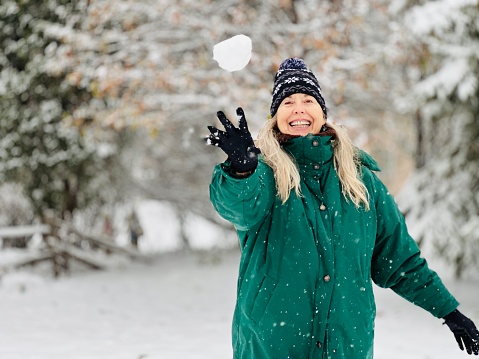 Senior woman throws snowball mid air to unseen person