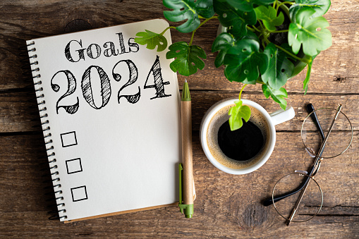 New year goals 2024 on desk. 2024 resolutions list with notebook, coffee cup on table. Goals, resolutions, plan, action, checklist concept. New Year 2024 template, copy space