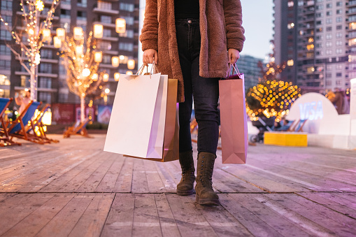 A young woman dressed in warm clothing is going Christmas shopping. The atmosphere is festive, and she is carrying shopping bags. Shopping for Black friday