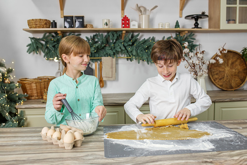 Two children prepare ginger cookies for Christmas holiday and play with cookie cutters.
