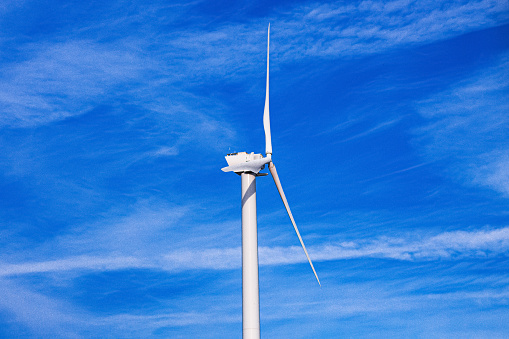 A white wind turbine with a blue sky background. The three large blades and the supporting tower are white.