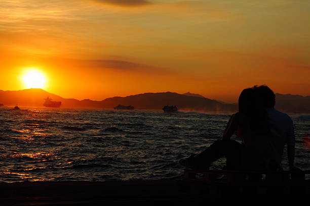Sweethearts sit watching the sunset at the seaside.