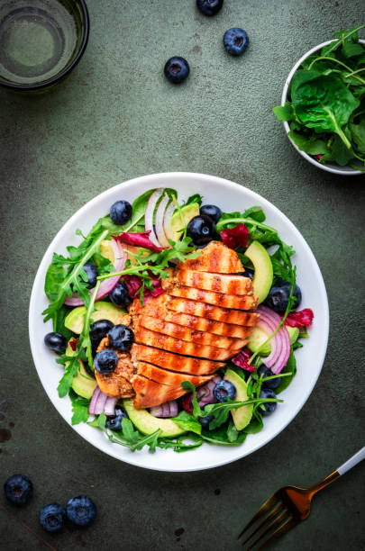 istock Fresh salad with blueberries, grilled chicken breast, avocado, red onion, walnuts and arugula on green table background, top view 1782834040