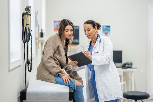 Senior female doctor listening to patient explaining her painful in her office. Mature woman doctor consulting patient in hospital room. Doctor and patient discussing health issue in office.