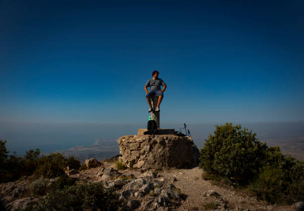 Man sitting on the summit marker with views of Alicante from Cabeçó d'Or mountain stock photo