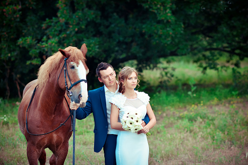 Stylish newlyweds stand near horse among the forest