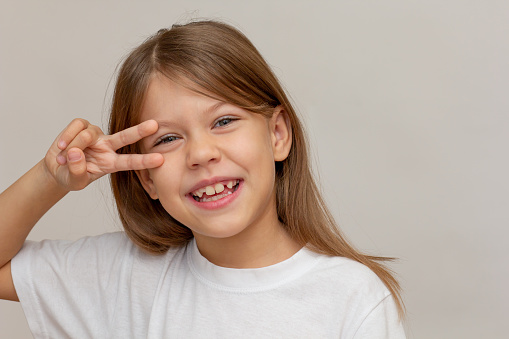Portrait of caucasian happy little girl with open wide smile making v sign near eyes looking at camera on white background