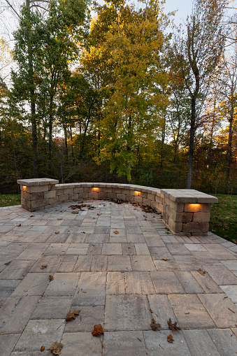 Picturesque backyard view in autumn season with patio pavers and stone wall, autumn leaves, and colorful woods in the background.