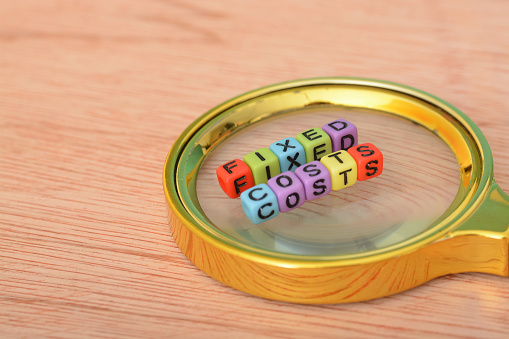 Magnifying glass with text FIXED COSTS. Fixed cost is a business expense that does not change regardless of the activity level of the business. Examples of fixed costs include rent, salaries, insurance, property taxes