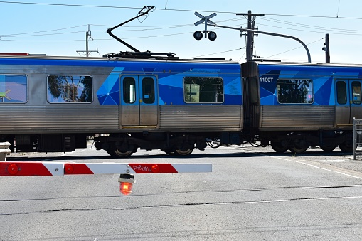 Melbourne, Victoria, Australia - October 03, 2022: A Metro train crosses a level crossing at Coburg North Station; illustrating the concept of transport infrastructure and danger at a road level crossing.