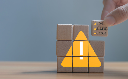 Developer programmer holding a wooden cube with warning triangle sign for notifying error found error and maintenance concept.