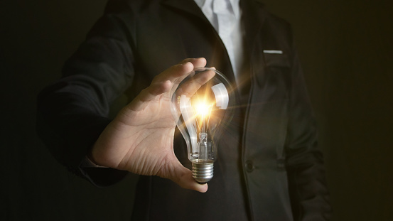 Innovative ideas and inspiration The hand of a male businessman holding a light bulb illuminates creative ideas with a glowing light bulb. Inspiration for sustainable business development ideas
