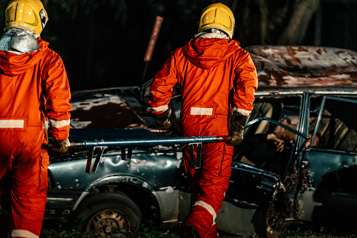 Two firefighters brining a man out of the car at night and placing him on the ground