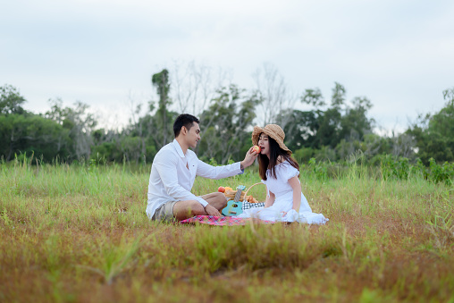 Asian couple having a picnic in the grass in the morning There are mountains and forests. Have fun and cheer during the holidays.