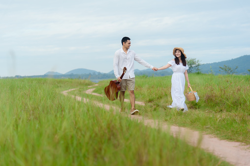 Asian man and woman couple walking in the middle of a meadow with a mountain background. morning sunlight