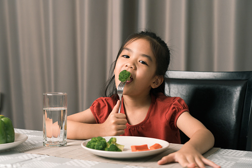 Asian little girl eating healthy vegetables with relish.