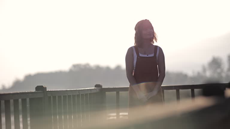Young beautiful woman greets the sun on the pier on Lake Efteni, The young woman's arms are stretched out by the lake, She opens her arms towards the sunrise, Beautiful young woman relaxing in nature