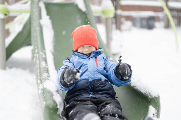 Brothers Sliding in the Snow Outdoors in Winter. They are smiling and having a lot of fun.