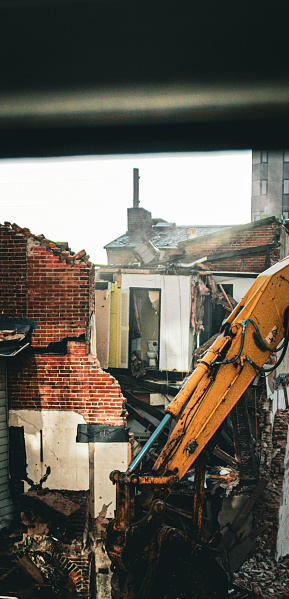 View from a window of a construction site destroying an old building, with bricks and all furniture inside with a huge crane claw