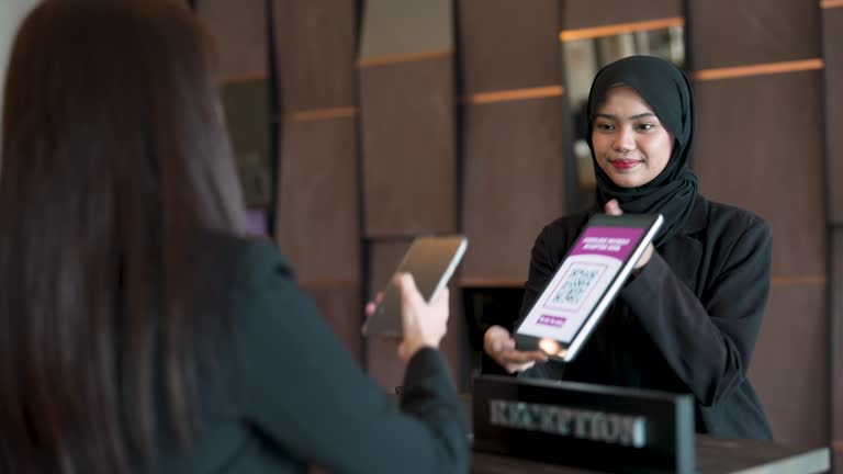 Asian businesswoman using smartphone for contactless payment at hotel reception