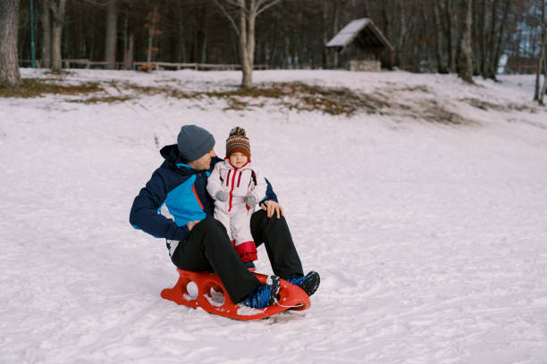 istock Smiling dad looking at little daughter sitting on sled on snowy plain 1783227123